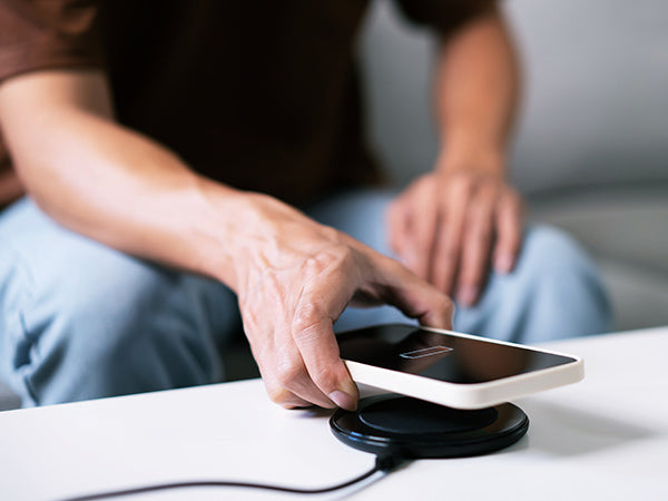 Hand placing white iPhone 17 on black wireless Qi2 charging pad with USB-C cable, demonstrating seamless fast charging for 2025 mobile setups.